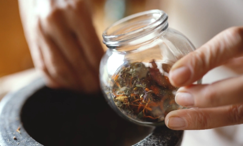 Ruka lagano prosipa suvu biljnu mešavinu iz tegle, kao deo prirodnog pristupa za ublažavanje nesanice