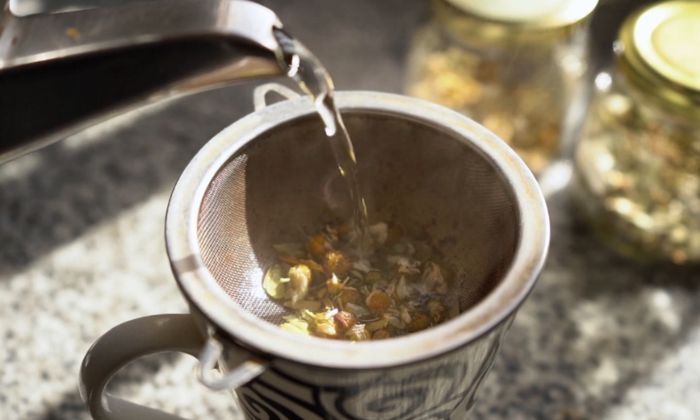 Vrela voda se lagano sipa preko mešavine suvog bilja u cedilu iznad šolje
