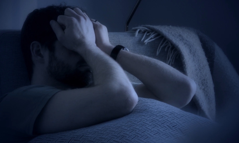 Muškarac sedi u zamračenoj sobi i drži glavu u rukama