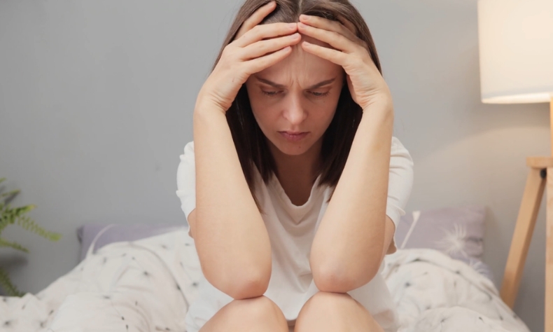 Žena sedi na krevetu i drži glavu rukama, iscrpljena i traži način za prirodno ublažavanje nesanice
