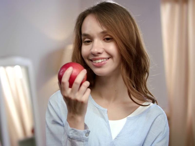 devojka drži crvenu jabuku u ruci i smeši se