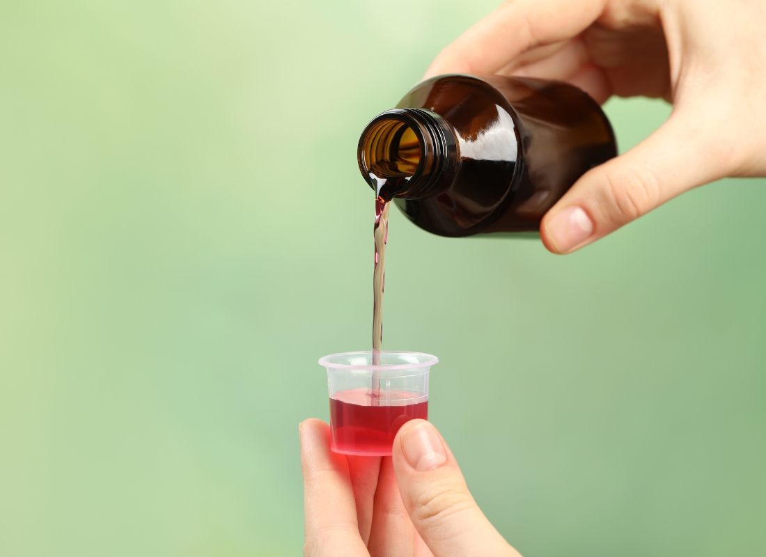 osoba sipa sirup z akašalj u čep, zelena pozadina