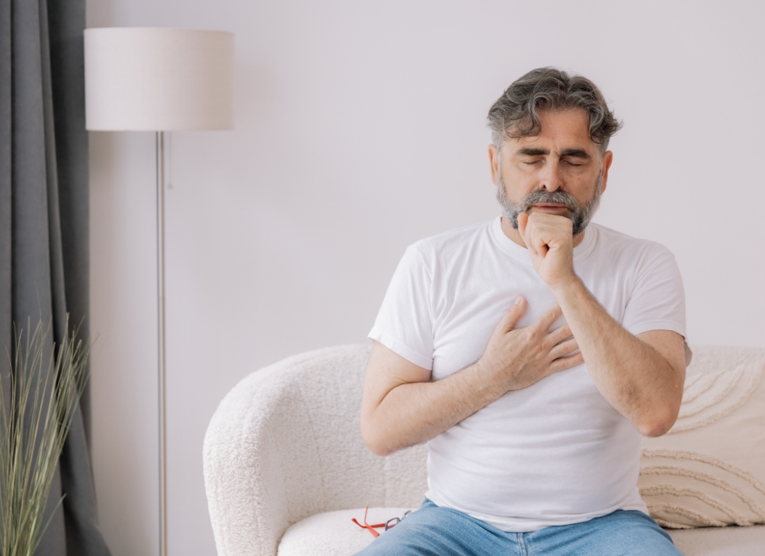 prikaz čoveka koji sedi na ugaonoj i kašlje, drži se za pluća